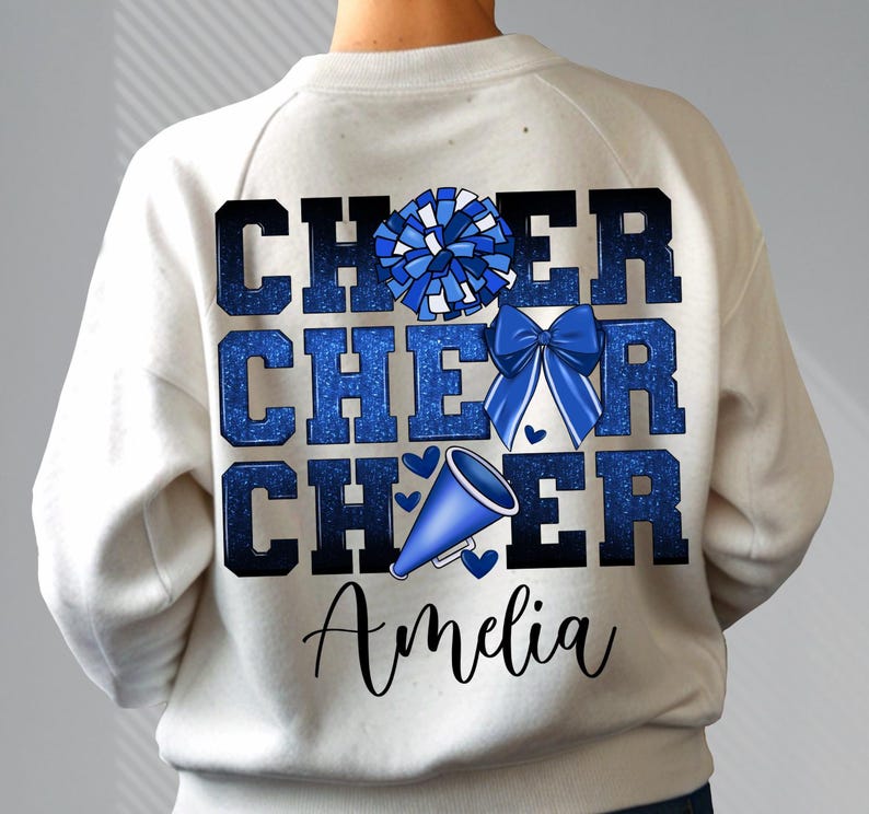 May include: White sweatshirt with blue glitter text that reads "Cheer Cheer Cheer" with a blue pom pom and a blue megaphone. The name "Amelia" is written in black below the text.