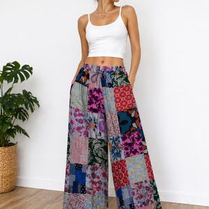 Może przedstawiać: Kobieta w białym topie na ramiączkach i spodniach palazzo w stylu patchwork. Spodnie mają r&oacute;żnorodne kolorowe wzory kwiatowe i geometryczne w odcieniach r&oacute;żu, niebieskiego, zielonego i czerwonego. Białe trampki dopełniają str&oacute;j.