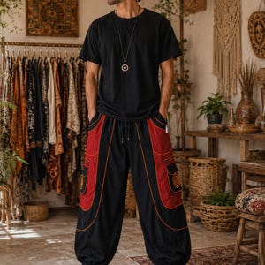 May include: A black short-sleeved t-shirt paired with loose-fitting black trousers featuring large red side panels, orange piping, and cargo pockets with circular graphic prints. The trousers have an elasticated waistband and cuffed ankles.