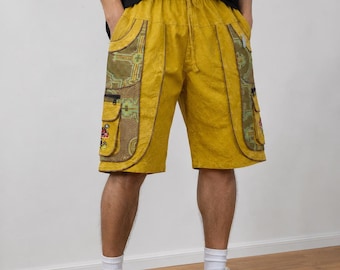 May include: Mustard yellow cargo shorts featuring an elastic waistband with a drawstring, two large side pockets with green and brown patterned fabric panels, black zipper closures, and small embroidered mushroom details on the lower pockets.