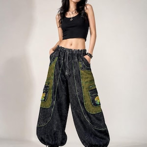May include: A black sleeveless crop top paired with loose-fitting, acid-wash black denim cargo trousers. The trousers feature large olive green side pockets with embroidered mushroom graphics, an elastic waistband with a drawstring, and black platform shoes.