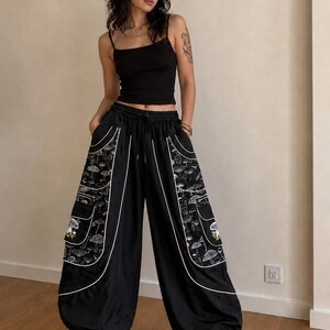 Puede incluir: Una camiseta de tirantes negra combinada con pantalones cargo negros de corte holgado. Los pantalones cuentan con grandes bolsillos laterales con estampado de setas blancas, ribetes blancos, cintura el&aacute;stica con cord&oacute;n y bajos ajustados.