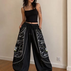 May include: A black spaghetti strap vest top paired with loose-fitting black cargo trousers. The trousers feature large side pockets decorated with a white line-art mushroom pattern, white piping accents, an elastic waistband with a drawstring, and cuffs.