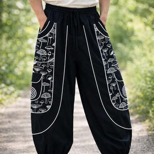 May include: Black loose-fitting trousers with an elastic drawstring waistband and cuffed ankles. The front features large side pockets decorated with a white line-art pattern of various mushrooms and spiral designs, outlined by white piping.