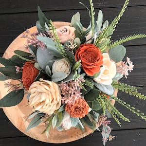 May include: A bouquet of faux flowers in shades of peach, cream, and burnt orange. The bouquet includes roses, eucalyptus, and other greenery.