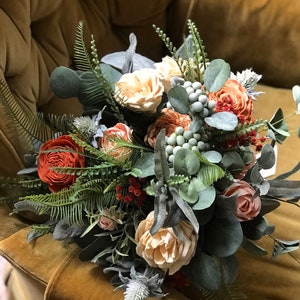 May include: A bouquet of faux flowers in shades of peach, orange, and green. The bouquet includes roses, eucalyptus, and other greenery.