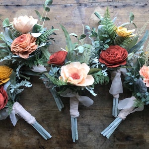 May include: Six small bouquets of faux flowers in shades of peach, orange, and red. The bouquets are made with silk flowers and greenery, and are tied with a simple ribbon.
