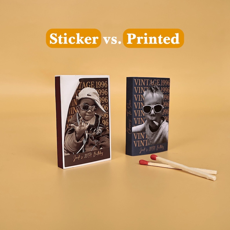 May include: Two rectangular matchboxes with custom photo designs labeled Sticker vs. Printed. One box features a peeling sticker showing a person in sunglasses, while the other has a direct print. Two wooden matches with red tips lie nearby.