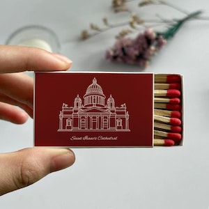 May include: A red matchbox featuring a white line drawing of Saint Isaac's Cathedral. The text "Saint Isaac's Cathedral" is below the illustration. The matchbox is open, revealing several matches with red tips.