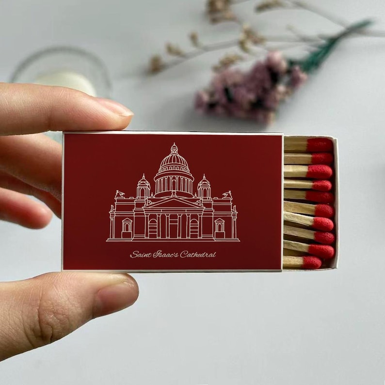 May include: A red matchbox featuring a white line drawing of Saint Isaac's Cathedral. The text "Saint Isaac's Cathedral" is below the illustration. The matchbox is open, revealing several matches with red tips.