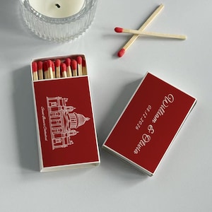 May include: Red matchbox with white text and a cathedral illustration. The box is open, revealing red-tipped matches. The closed box has the names "William & Olivia" and the date "08.12.2026".