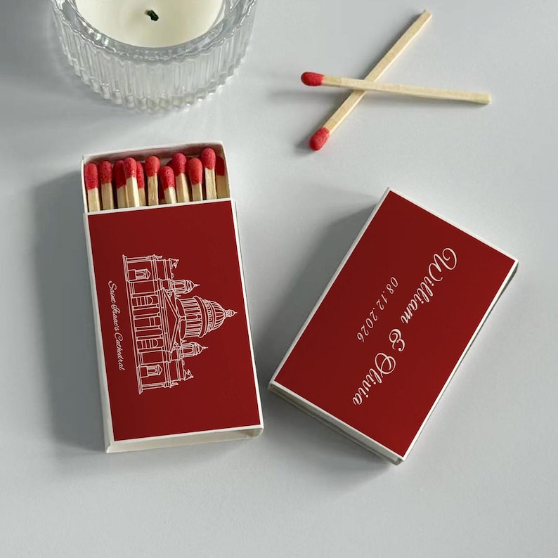 May include: Red matchbox with white text and a cathedral illustration. The box is open, revealing red-tipped matches. The closed box has the names "William & Olivia" and the date "08.12.2026".
