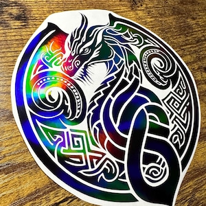 May include: A black and iridescent vinyl sticker featuring a Celtic knot design with a dragon in the center. The dragon is facing left and has a detailed design.