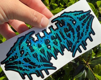May include: A rectangular sticker featuring a stylized, symmetrical graphic design in a bright, glittery cyan blue color. The artwork consists of intricate, web-like black lines layered over the shimmering blue surface, creating a sharp, jagged aesthetic.