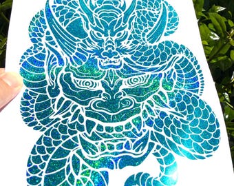 May include: A teal and blue glitter decal featuring a detailed dragon head surrounded by a coiled, scale-patterned serpent body. The design is printed on a white sheet, showcasing a vibrant, shimmering finish with intricate line work throughout.