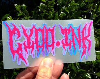 May include: A rectangular sticker featuring the text GYDD.INK in a stylized, dripping, heavy metal-inspired font. The lettering is vibrant pink with a light blue outline, set against a semi-transparent, frosted white backing material.