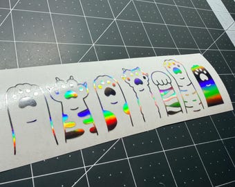 May include: A rectangular sticker sheet featuring seven distinct cat paw designs in a holographic finish. Each paw is rendered in a simple line art style with varying patterns, including stripes and spots, reflecting a rainbow spectrum of colors.