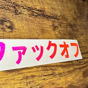 May include: A white sticker with the Japanese text "ワックオフ" in pink and red lettering.