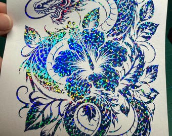May include: A holographic blue decal featuring a detailed dragon winding around a large hibiscus flower. The design is composed of intricate lines and scales with a reflective, multi-colored glitter effect on a white backing sheet.