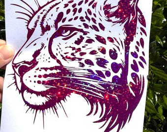 May include: A decal featuring a profile view of a leopard head. The design is rendered in a deep magenta color with a prominent glittery, holographic finish that catches the light. The leopard is depicted with detailed spots and whiskers.