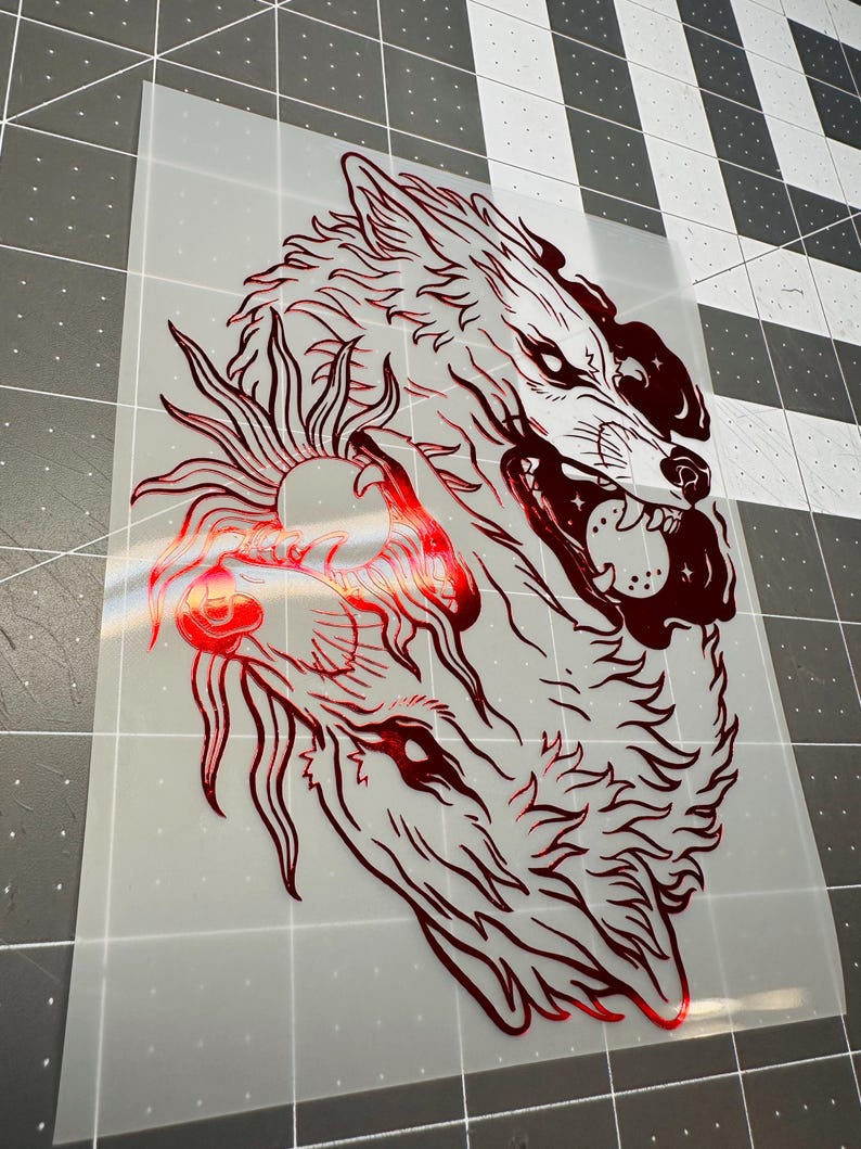 May include: A red graphic of two wolves, one snarling with bared teeth, and the other with a sun-like design. The image is on a transparent background, suitable for heat transfer vinyl or similar applications.