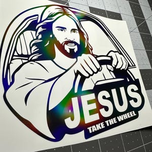 May include: A white sticker featuring an illustration of Jesus driving a car. The image has a rainbow holographic effect. The text "JESUS TAKE THE WHEEL" is displayed in bold white letters.