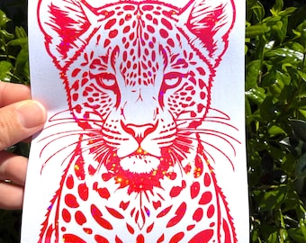 May include: A rectangular white sticker featuring a vibrant hot pink leopard illustration with a holographic finish. The design displays the head and upper chest of a leopard with detailed spots, whiskers, and intense eyes, rendered in a bold graphic style.