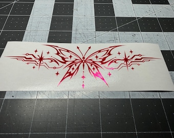 May include: A red vinyl decal featuring a symmetrical butterfly design with sharp, angular tribal-style wings. The graphic includes multiple four-pointed star accents and thin, geometric lines extending horizontally from the central butterfly body.