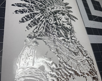 May include: A metallic silver foil print on a white sheet featuring a detailed illustration of a person wearing a traditional feathered headdress and ornate jewelry. The artwork displays intricate line work and reflective textures throughout.