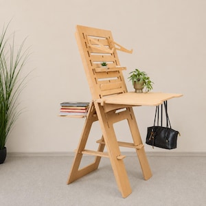 Peut inclure: Un bureau debout en bois clair doté d'un haut panneau arrière rainuré avec des étagères réglables, une surface de travail principale et une plateforme latérale. Une pile de livres est posée sur le côté, avec une petite plante et un sac à main noir.