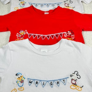 May include: Three white t-shirts with embroidered Disney characters and names. The top shirt has Mickey Mouse and the name Peyton. The middle shirt has Donald Duck and the name Theodore. The bottom shirt has Donald Duck and Mickey Mouse and the name Wright.