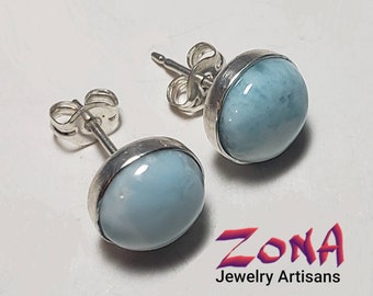 May include: A pair of silver stud earrings with light blue oval-shaped gemstones. The earrings are set in a silver bezel setting.
