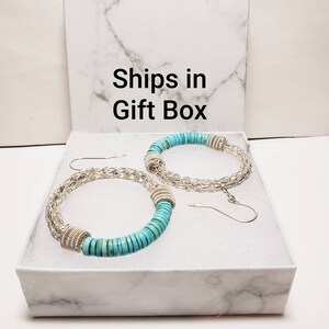 May include: A pair of turquoise and silver hoop earrings in a white gift box. The earrings are made with turquoise stones and silver chain links. The box has the text "Ships in Gift Box" printed on the top.