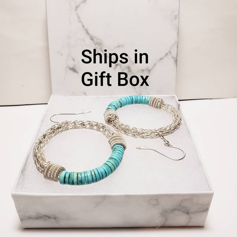 May include: A pair of turquoise and silver hoop earrings in a white gift box. The earrings are made with turquoise stones and silver chain links. The box has the text "Ships in Gift Box" printed on the top.