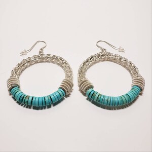 May include: A pair of silver hoop earrings with turquoise beads. The earrings are made of a woven wire design and have a turquoise bead accent.