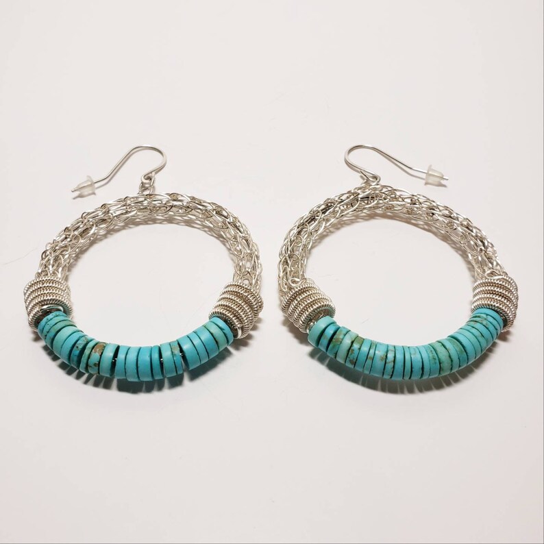 May include: A pair of silver hoop earrings with turquoise beads. The earrings are made of a woven wire design and have a turquoise bead accent.