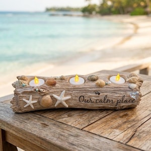 May include: A rectangular driftwood-style candle holder featuring three circular cutouts for tea lights, decorated with various seashells and starfish. The text "Our calm place" is inscribed on the front surface in a dark, cursive script.