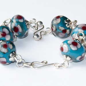 May include: A silver chain bracelet with turquoise blue beads decorated with white and red flowers.