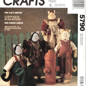 Op de afbeelding: Een McCall's Crafts naaipatroon-envelop 5790 met instructies voor het maken van drie gevulde stoffen kattenpoppen, elk 53 cm lang. De hoes toont illustraties van de katten in verschillende outfits, waaronder tuinbroeken en jurken.