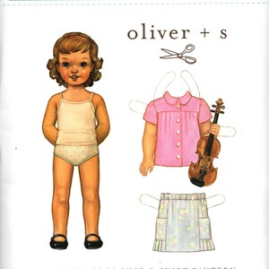 May include: A sewing pattern envelope for a music class blouse and skirt by oliver + s. The cover features an illustration of a paper doll, a pink button-down blouse, a floral skirt, and a violin. The text reads SIZES: 5, 6, 7, 8, 10, + 12.