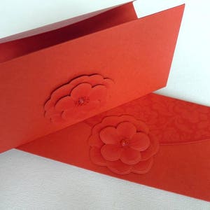 May include: Two red envelopes with a 3D flower design. The envelopes are folded and have a textured surface.