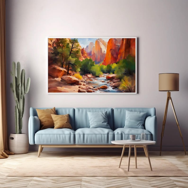 May include: A framed watercolor painting depicts a canyon landscape with red rock formations, a flowing river, and green trees. The artwork hangs above a light blue sofa with throw pillows. A cactus and a floor lamp are also in the room.