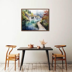 May include: Watercolor painting of a waterfall scene with a wooden bridge. The artwork features a brown wooden frame, a river, and lush greenery. The painting is displayed above a dark wooden table with two chairs.