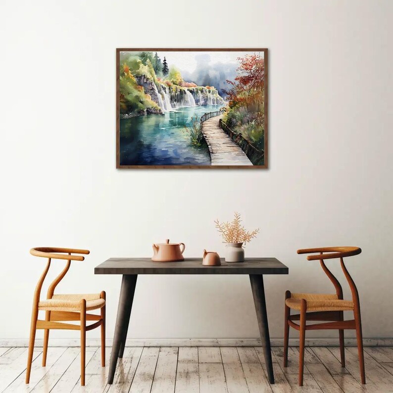 May include: Watercolor painting of a waterfall scene with a wooden bridge. The artwork features a brown wooden frame, a river, and lush greenery. The painting is displayed above a dark wooden table with two chairs.