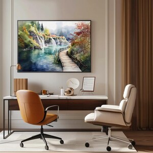 May include: A framed watercolor painting depicts a serene landscape with a waterfall, a wooden walkway, and lush greenery. The painting hangs above a modern desk with two office chairs, one tan and one cream-colored.