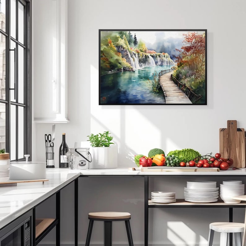 May include: A framed watercolor painting depicts a scenic waterfall cascading into a blue lake. A wooden walkway extends into the water, surrounded by lush greenery and autumn foliage. The artwork is displayed on a white wall in a kitchen setting.