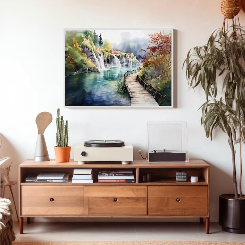 May include: Watercolor painting of a waterfall scene with a wooden walkway. The artwork features a vibrant color palette of blues, greens, and autumn hues. The painting is framed and displayed above a wooden console with a record player.