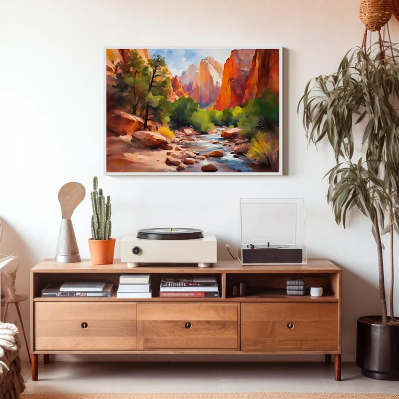 May include: A framed watercolor painting of a canyon landscape with a river, trees, and mountains. A wooden media console with a record player, cactus, and decorative items sits below the painting.