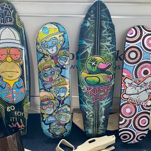 May include: Four colorful skateboards with different designs. The first skateboard has a cartoon character with a yellow face and blue shirt. The second skateboard has a monkey design with the words "No Monkey" on it. The third skateboard has a green rubber duck with the words "Rubber Duck" on it. The fourth skateboard has a black and white monkey design with the word "Monkey" on it.