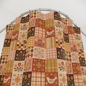 May include: A shower curtain featuring a patchwork design of squares with various patterns including tulips, birds, hearts, and plaid in shades of brown, orange, pink, and cream, suspended from a curved metal rod with silver-colored rings.